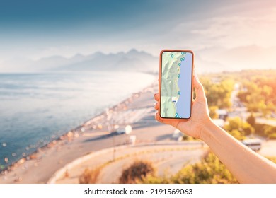 Hand with screen of smartphone with working maps and geolocation with checkpoints against background of Scenic beach in Antalya resort town. Travel applications and digital guide concept - Shutterstock ID 2191569063