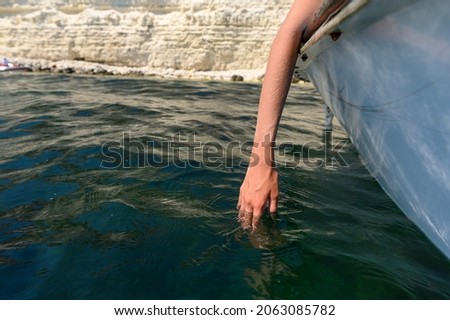 Hand in sea water from a boat on the background of rocks.