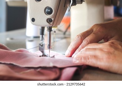 Hand of seamstress using industrial sewing machine to sew the seams of pink cloth close-up.