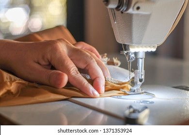 Hand of the seamstress is using a white industrial sewing machine to sew yellow cloth.