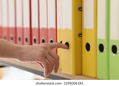 Hand of secretary taking yellow ring binder with documents. Organized structure of colorful folders with archive files put in row on shelf