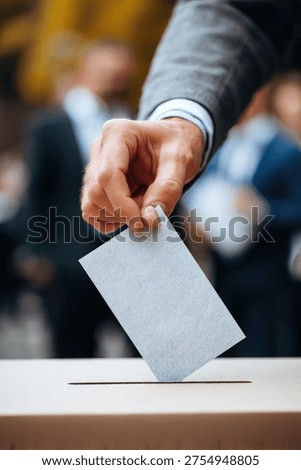 A hand is seen casting a vote into a ballot box, symbolizing the democratic process of elections and civic participation.