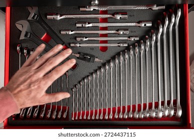 Hand selecting a tool from an organized workshop drawer filled with neatly arranged wrenches, showing order choice and professional tool storage
