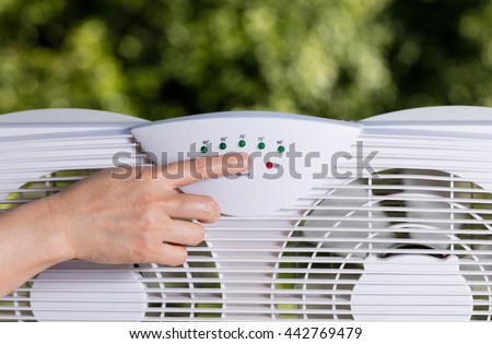 Hand selection temperature on two way window fan in home window with blurred out trees in background. 