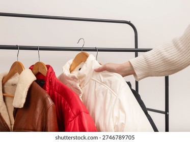 Hand selects jacket from metal rack against white background. Assorted outerwear rests on wooden hangers along black rail. Minimalist retail fashion concept for wardrobe choice in boutique shop