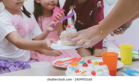 Hand Is Sending Birthday Cake To Children During Celebrating, Birthday Holiday. Cheerful Children, Friends Having Fun And Eat Cake On Table At Modern Room. Childhood, Friendship Concept