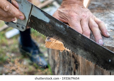 The hand of a senior man is sawing a board with an old hand saw or hacksaw. In the close-up photo, only a part of the saw and the hand.