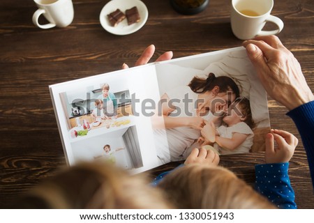 Hand senior woman and child holding a family photo album against the background of the a wooden table.