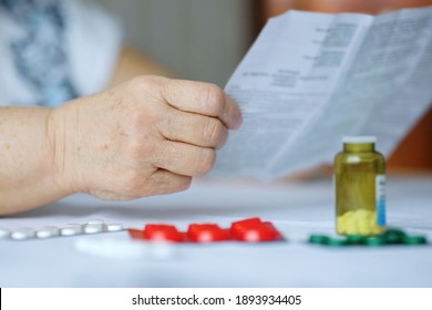 Hand Of Senior Woman Holding Leaflet To Prescribed Medicine, Pills Lying Beside On Table. Closeup Patient Reading Information Sheet. Concept Of Healthcare