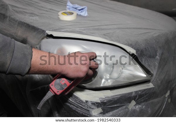 The hand of\
the serviceman matting an old worn headlight with a grinder before\
polishing it, car body repair\
service