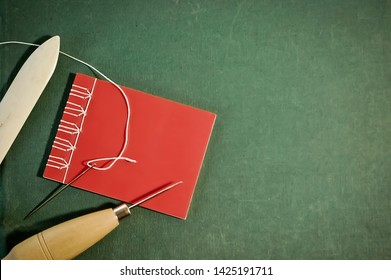 Hand Sewn Red Notebook with Bookbinding Tools on Green Background