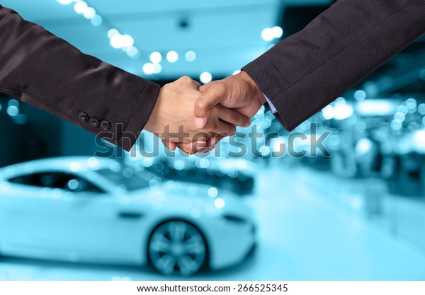 Hand shake between a\
businessman and a businesswoman on abstract blurred photo of motor\
show background