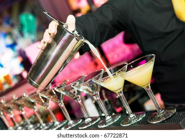 Barman?s Hand With Shake Mixer Pouring Cocktail Into Glasses Arranged In A Line