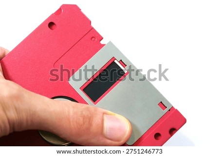 Hand showcasing a red floppy disk magnetic surface, closeup of vintage data storage media and retro technology, old school file backup concept, obsolete magnetic diskette