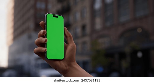 Hand showcasing a smartphone with a green screen on an urban city street background, perfect for digital nomads and a vibrant lifestyle - Powered by Shutterstock