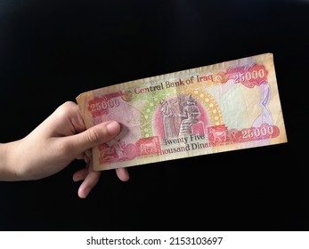 Hand Showing 25000 Iraqi Dinar Note Money From Central Bank Of Iraq Over Black Background And Selective Focus

