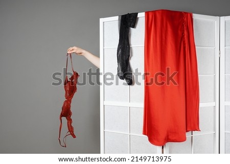 hand showing bra while hidden woman is undressing behind folding screen