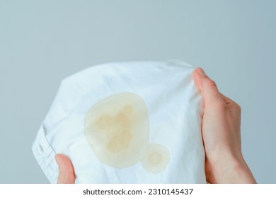 Hand showing dirty souce cosmetic stain on white shirt. Visual evaluation of stains on clothes. Liquid yellow stains. daily life stain concept. High quality photo - Shutterstock ID 2310145437