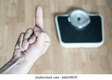 Hand Showing Middle Finger To Weight Scale. Flipping The Bird. Man Frustrated And Angry From Being Overweight And Obese. Problem And Failure In Weight Loss. No Results And Unsuccessful Person.