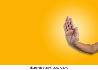 A hand showing an obstructing gesture, with an open palm facing forward on a yellow background. - Shutterstock ID 2009773091