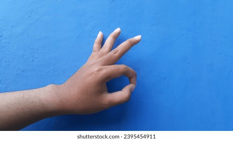 A hand showing an ok gesture isolated on a blue wall background. Okey hand sign. - Shutterstock ID 2395454911