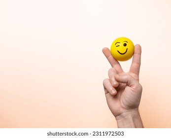 Hand showing the victory symbol with an emoticon between the fingers which winks at the camera. Victory and success concept.
