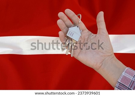 Hand shows the keys to the apartment on background of flag Latvia. Keys to the apartment in a female hand on background of flag Latvia. Realty concept and home buying or new apartment in Latvia