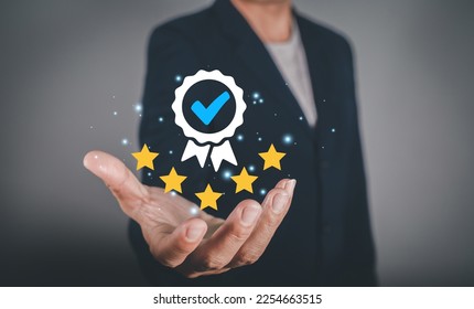 Hand shows the sign of the top service Quality assurance, Guarantee, Standards, ISO certification and standardization concept. Approved badge icon symbol medal award ribbon with 5 stars. - Shutterstock ID 2254663515