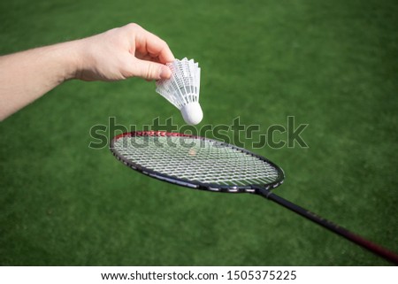 Hand with shuttlecock on a background of grass, a racket near. Serving in badminton. The concept of summer hobbies, outdoor activities, amateur badminton, sports.