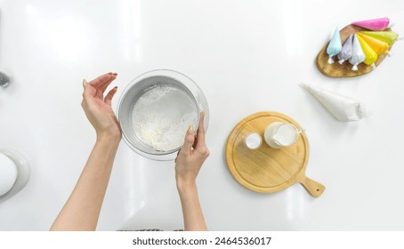 Hand sifting flour in a kitchen with baking ingredient and colorful icing on the side. Top view - Powered by Shutterstock