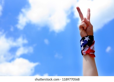 Hand with sign of victory with american USA flag tied on wrist on blue sky background. Victory and Independence day concept.