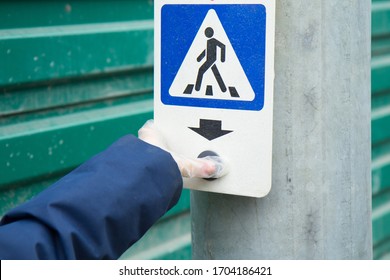 A hand in a silicone glove presses the crosswalk button. Protection on the street during the coronavirus pandemic. Pedestrian crossing sign.