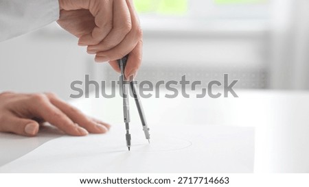 A hand skillfully uses a compass to draw precise circles on a sheet of white paper in a bright setting.