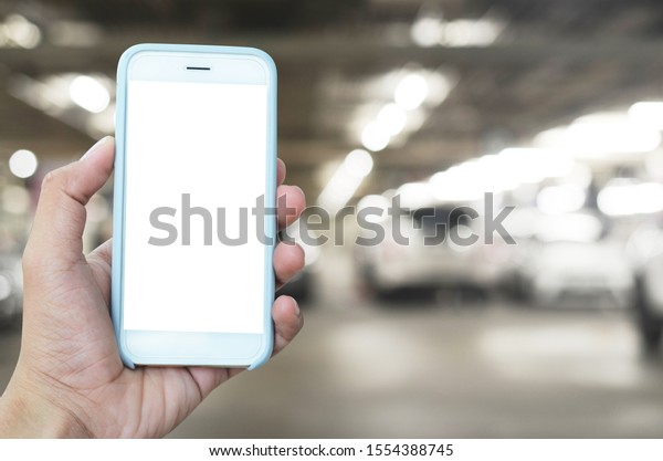 Hand with Smart phone with blank screen at\
parking area. Mock up image, man hands holding mobile smart phone\
in indoor car parking.