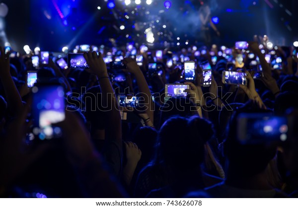 スマートフォンを持つ手とライブ音楽祭 コンサートのステージ ライブコンサート 音楽祭 幸せな若者 豪華なパーティー 風景の外観の写真を撮る の写真素材 今すぐ編集