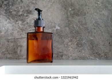 Hand Soap Dispenser In A Brown Glass, Square Bottle, With Black Pump, And Grey Marble Backsplash Near Kitchen Sink