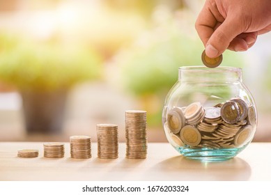 Hand Of Someone Put Coin To Glass Money Box With Step Of Growing Coins, Money Saving Or Investing For Home Lone Or Real Estate Concept