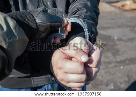 the hand of a special forces soldier puts handcuffs on the hands of a detained, captured, arrested bandit, offender