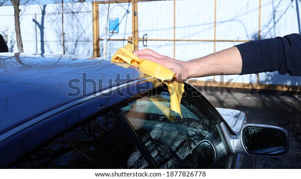 a\
hand with a special yellow suede cloth wipes the body of a silver\
car, cleanly washed at home, a backyard flooded with sunlight\
against the background of a gray fence with a\
mailbox