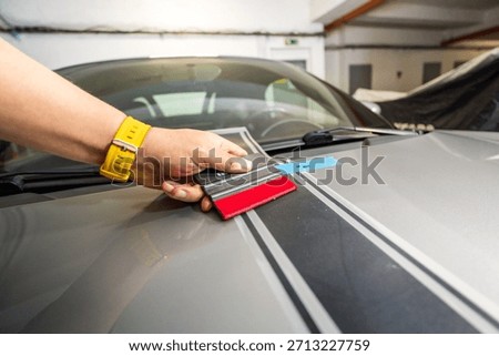 Hand of a specialist installing decals. Application of a black foil sticker on the hood of a sports car. Decal installation.