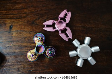 Hand Spinners Or Fidgeting Spinners. Various Types And Shapes Of Spinners Put On The Wooden Background. A Toy For Hyperactive Child Therapy.