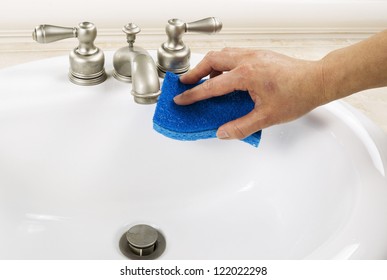 Hand With Sponge Cleaning Bathroom Sink Faucet