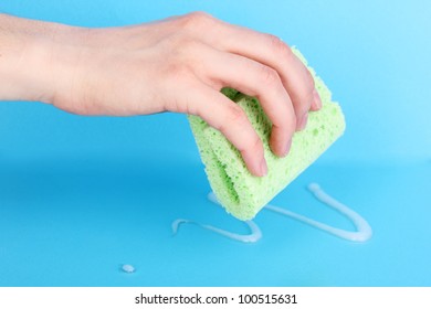 Hand with sponge and poured detergent on blue background - Shutterstock ID 100515631