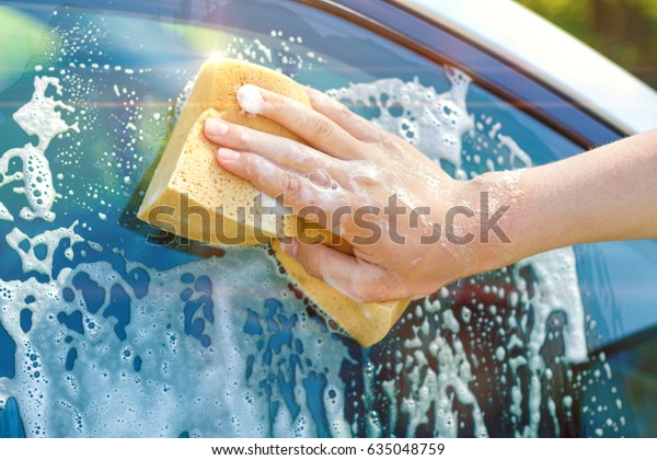 A hand\
with a sponge washes the window of a\
car.