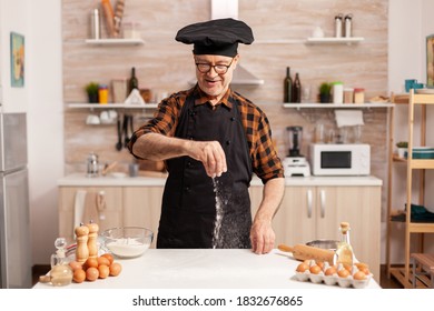 Hand spreading wheat flour on wooden kitchen table for homemade pizza. Retired senior chef with bonete and apron, in kitchen uniform sprinkling sieving sifting ingredients by hand. - Powered by Shutterstock