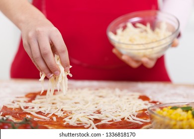 Hand sprinkle grated cheese from a bowl on a half prepared pizza - close up, shallow depth - Powered by Shutterstock