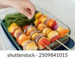 Hand sprinkling salt on vegetable skewers in a glass dish