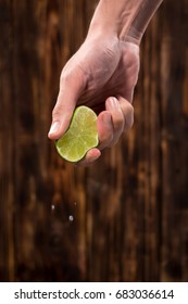 Hand squeeze lime with lime drop on dark wooden background
