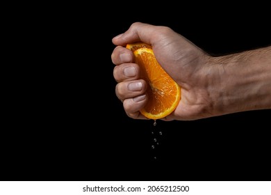 Hand squeezes juice from an orange on a black background. Fresh and juicy orange