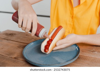 Hand squeezes ketchup onto a hot dog sausage in a hot dog bun, fast food breakfast - Powered by Shutterstock